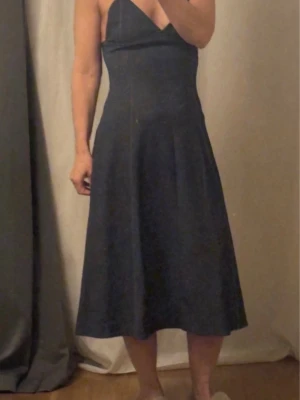 Zara Mörkblå axelbandslös klänning - Snygg strechig jeans klänning med v-ringad urringning och smala axelband. Klänningen har en figurnära överdel och ett utsvängt kjolparti som ger en elegant siluett. Perfekt för dig som gillar minimalistisk och stilren design.