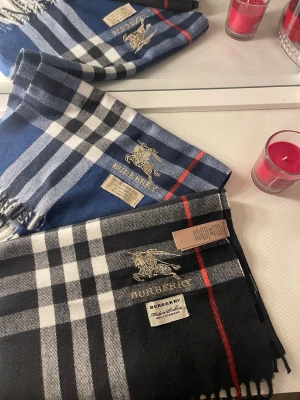  rutig halsduk i kashmir - Säljer två klassiska rutiga halsdukar i 100% kashmir. En i svart, vit och röd samt en i blå, vit och röd. Båda har broderad och fransar i ändarna. Perfekt accessoar för att lyfta din outfit. Två kostar 1000 en 600kr