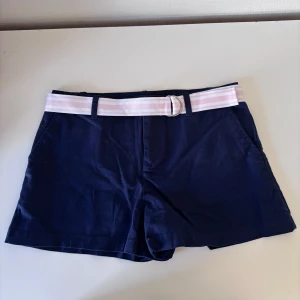 Marinblå shorts med rosa bälte - Snygga lågmidjade marinblå shorts med ett randigt rosa och vitt bälte. 