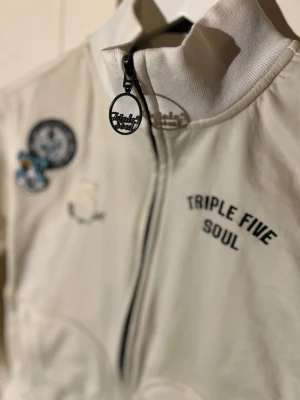 Vintage ziptröja Triple Five Soul - Vintage ziptröja med dragkedja från Triple Five Soul. Inköpt i New York 90-tal , så endast ett fåtal plagg finns kvar från kollektion år 99-2000 . Det är fint  broderade patches och siffran 5 på bröstet samt svart text. Ståkrage och coolt rundat dragkedjehänge. Perfekt för en streetwear-look.
