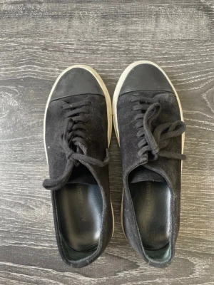 Svarta Axel Arigato - Stilrena svarta sneakers från Axel Arigato med ovandel i mocka och tåparti i svart gummi. Skorna har vita sulor och svart snörning.