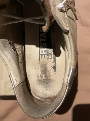 Golden Goose Superstar sneakers beige/brun - Golden Goose Superstar sneakers i beige och brunt med ikonisk stjärndetalj på sidan. Ovandel i läder och mocka, vita skosnören och högt skaft. Märkeslapp på plösen och vintageinspirerad design. Perfekta för dig som gillar streetstyle och unika detaljer.