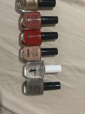 Nagellackspaket från NOBÉ - Säljer ett paket med sex nagellack från NOBÉ i olika färger: guld, korall, röd, nude, grå och ett genomskinligt topplack. Flaskorna har klassisk form och svarta lock. Perfekt för dig som vill variera din nagelstil med trendiga färger.