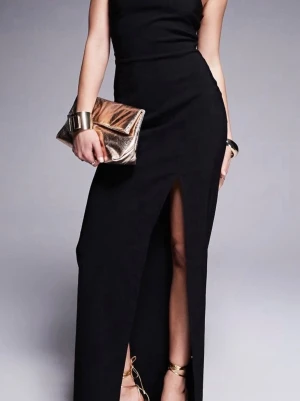 Svart långklänning med slits - Elegant svart långklänning med hög slits framtill och ärmlös design. Klänningen har en figurnära passform och dragkedja i ryggen. Perfekt för dig som vill ha en stilren och klassisk look.