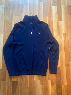 Gant stickad tröja - Mörkblå stickad tröja från Gant med halv dragkedja och liten logga broderad på bröstet. Den är sparsamt använd och har inga problem. Storlek M men passar både S och M.