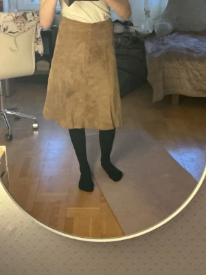 Beige mockakjol från H&M - Snygg beige mockakjol från H&M i en klassisk A-linjeform. Kjolen har en mjuk yta och är perfekt för en stilren look. Passar bra till både vardag och mer uppklädda tillfällen.