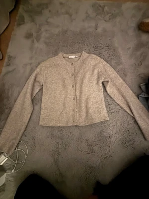 Beige kofta från Kappahl - Mysig beige kofta från Kappahl i storlek XS. Koftan har rund halsringning, knappar framtill och är ribbstickad vid ärmslut och nederkant. Perfekt att slänga över en topp för en enkel och clean look.