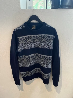 Mörkblå stickad tröja från C&A Empire - Säljer en mörkblå stickad ulltröja från C&A Empire i Shetland wool. Klassisk vintage-modell med ljusgrått mönster över bröstet. Varm och skön tröja i 100% ren ny ull. Perfekt till höst och vinter. Tröjan är använd och har ett litet hål på ryggen (se bild), men annars i bra skick och fortfarande fullt användbar. Storlek: L (52/54) Material: 100% ull Färg: Mörkblå / grå Skriv gärna om du har frågor!