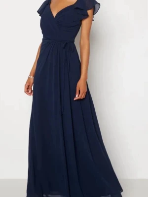 Marinblå balklänning med v-ringning - Elegant marinblå långklänning med v-ringad omlottdesign och korta volangärmar. Klänningen har markerad midja med knytband och ett flytande, svepande fall. Perfekt för dig som vill ha en stilren och klassisk look.
