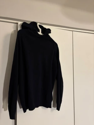 Marinblå hoodie från Oscar Jacobsson - En stilren marinblå hoodie med huva och långa ärmar. Hoodien har en klassisk passform utan tryck eller mönster, perfekt för en clean och avslappnad look. Tillverkad i mjukt material som känns skönt mot huden.