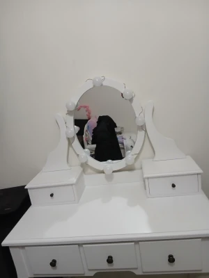 Vit sminkspegel med lampor - Stilren vit sminkspegel med rund spegel omgiven av dekorativa lampor för extra belysning. Spegeln är monterad på ett sminkbord med flera lådor för förvaring av smink och tillbehör. Klassisk design i trä som passar perfekt i sovrummet eller sminkhörnan.