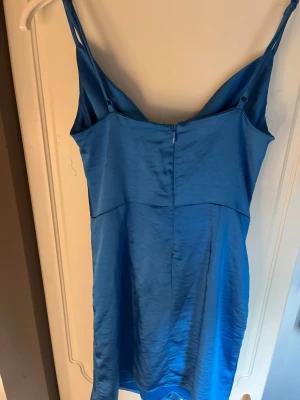 Blå satin klänning Gina Tricot - Snygg blå klänning från Gina Tricot i satinliknande material. Klänningen har smala axelband, figurnära passform och dragkedja bak. Perfekt för dig som vill ha en enkel men stilren look.