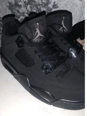 Svarta Air Jordan 4 Retro sneakers - Säljer ett par svarta Air Jordan 4 Retro sneakers med klassisk Jumpman-logga på plösen och häl. Skorna har snörning, meshdetaljer på sidorna och tåboxen samt detaljer i syntet och mocka för en clean och sportig look.