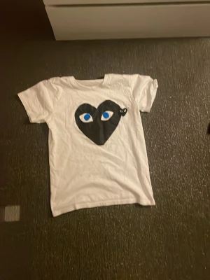 Vit Comme des Garçons Play t-shirt - Vit t-shirt från Comme des Garçons Play med tryck. Skön t-shirt som passar inför sommaren/våren och väldigt clean! Trycket är lite urtvättat men inget jättefarligt! Hör av dig för fler bilder! 