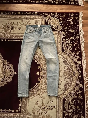 Ljusblå slim fit jeans från 157 lagar - Säljer ett par ljusblå slim fit jeans från lagar 157 med klassisk femficksdesign och normal midja. Jeansen har en snygg tvättad look och raka ben. Perfekta för dig som gillar en enkel och stilren stil.