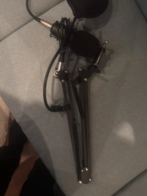 Svart mikrofon med arm och popfilter - Säljer en svart mikrofon med tillhörande justerbar arm och popfilter, perfekt för streaming, podd eller gaming. Mikrofonen har metallfäste och flexibel arm som enkelt kan monteras på skrivbord. Popfiltret hjälper till att minska störande ljud vid inspelning.