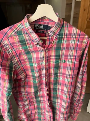 Rosa Rutig skjorta från Polo Ralph Lauren - Säljer en färgglad rutig skjorta från Polo Ralph Lauren i slim fit-modell. Skjortan har knappar hela vägen, klassisk krage och lång ärm. Färgerna går i rosa, grön, vit och inslag av blått. Inga fel på den. 