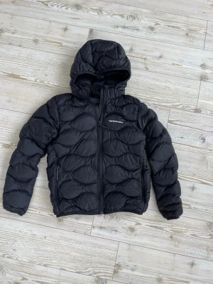 Svart pufferjacka från peak performance  - Snygg svart pufferjacka från peak performance med snygg design över hela jackan. Storlek 160. Jackan har ett hål som har sytts igen på ena armen.