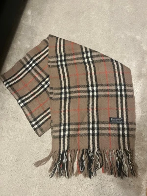  halsduk från Burberry -  halsduk från Burberrys i 100% lammull.  Säljer snabbt då den inte kommer till användning, kom gärna med prisförslag för snabb affär!