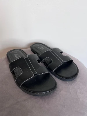 Svarta slip-in sandaler från Lager157, storlek 39 - Svarta slip-in sandaler från Lager157 med breda remma, vita kontrastsömmar, öppen tå och rektangulära utskärningar på ovandelen. Tillverkade i konstläder. Använda en gång.