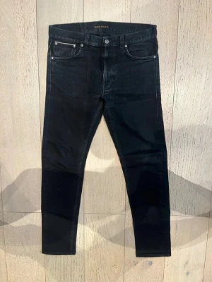Svarta slim fit  jeans från Nudie Jeans - Snygga svarta skinny jeans från Nudie Jeans med klassisk femficksmodell och silverfärgade nitar. Jeansen har en smal passform och är tillverkade i stretchigt denimtyg för extra komfort. Perfekta för en stilren och modern look.