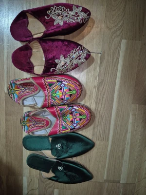 Tre par marockanska slip-ins  - Säljer tre par orientaliska / marockanska slip-ins i satin, ett par i vinrött med broderade blommor och pärldetaljer, och ett par i mörkgrönt med tofsar och små pärlor. Båda har spetsig tå och låg klack, perfekta för dig som gillar unika skor med snygga detaljer.