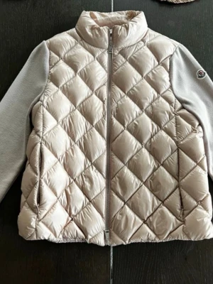 Beige dunväst från Moncler -  Quiltad skaljacka storlek S Detaljer - ljusrosa - dragkedja fram - två passpoalfickor i sidan Material Foder: polyamid 100%,  gåsdun 90%,  fjädrar 10% Yttre: polyamid 100%,  jungfruull 100%  Nypris just nu: 11 700 på Monclers sida!   Köpt i monclers butik i Oslo! Bild på kvitto finns på sista sliden.  Jackan ser grå ut på vissa bilder men är LJUSROSA i verkligheten, se alla bilder för bättre färg på jackan! De sista bilderna visar en logga man får med cardiganen!💞💞