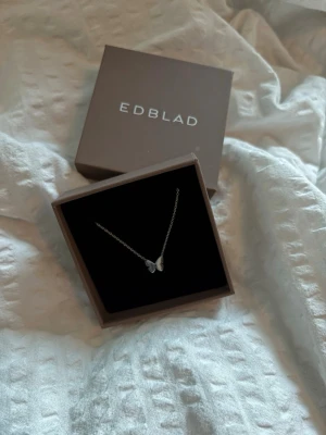 Silverhalsband med fjäril från Edblad - Snyggt silverfärgat halsband från Edblad sopm har ett hänge i form av en stilren fjäril. Kedjan är tunn och elegant, perfekt för dig som gillar minimalistiska smycken. Kommer i original ask från Edblad.