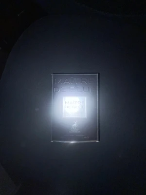Maître De Blue parfym Alhambra - Maître De Blue från Alhambra är en elegant parfym i en mörkblå, fyrkantig glasflaska med svart lock. Förpackningen har en stilren design med silvertext. Perfekt för dig som gillar exklusiva och moderna dofter. 