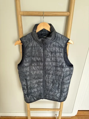 Uniqlo Vest *XS* - Snygg mörkgrå dunväst från Uniqlo med hög krage och dragkedja framtill. Västen har en quiltad design och två sidofickor. Perfekt att slänga över en hoodie eller tröja för extra värme. Lätt och smidig att bära med sig.