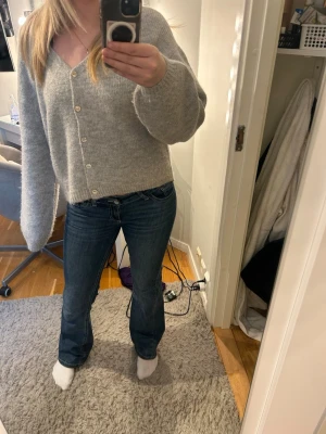 Grå stickad kofta från Gina Tricot - Mysig grå stickad kofta från Gina Tricot i ullblandning. Koftan har v-ringning, långa ärmar och knäppning framtill med ljusa knappar. Perfekt för lager på lager och enkel att matcha med jeans eller kjol.