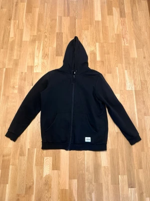 Svart hoodie med dragkedja från Stussy - Svart hoodie från Andy’s med dragkedja framtill och två stora fickor. Klassisk huva och ribbade muddar vid ärmslut och nederkant. Perfekt för en avslappnad streetwear-look. Säljer en svart Andy’s zipper Hoodie! Den är fin och är i väldigt bra skick! Ganska stor, är i storlek XXL. Säjer för 150kr, skriv vid funderingar:)!