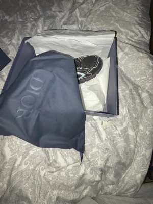 Svarta Dior sneakers med vita detaljer - Säljer ett par svarta Dior sneakers med vita och grå detaljer. Skorna har en chunky sula och sportig design med tydliga Dior-loggor på sidan. Materialet är en mix av mesh och läder för både stil och komfort. Perfekta för dig som vill sticka ut med exklusiva sneakers. Tar även emot byten mot vita b30 elle b22 DM för mer bilder