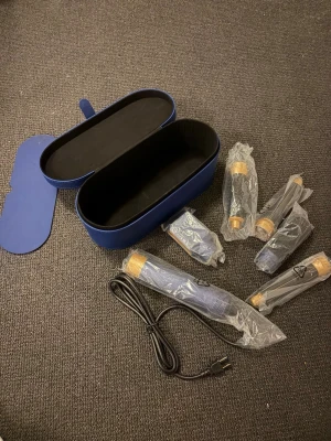 Dyson Airwrap hårstyler med tillbehör - Säljer en blå Dyson Airwrap hårstyler med flera olika stylingtillbehör och originalförvaringsväska. Inkluderar borstar och locktillbehör i plast och metall samt laddningskabel. Perfekt för att skapa olika frisyrer med stil, priset kan sänkas vid snabb affär.