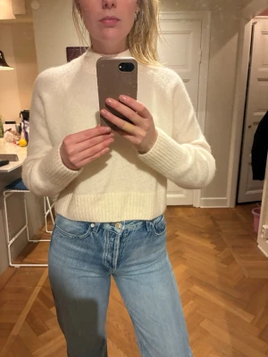 Vit stickad tröja - Mysig vit stickad tröja i ull från & Other Stories med hög hals och ribbade muddar vid ärmslut och nederkant. Tröjan har en rak passform och är perfekt att styla med jeans. Materialet ser mjukt och fluffigt ut, vilket ger en skön känsla. Inga synliga loggor eller mönster.