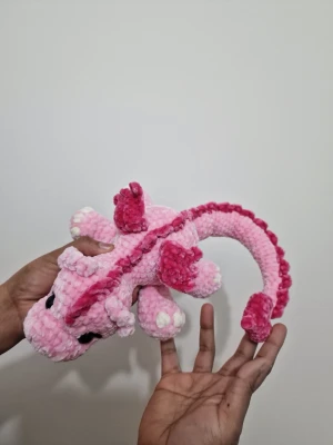 Rosa virkad drakmjukis- fairy valentine dragon  - Söt handgjord drake i mjuk virkad plysch, rosa med mörkrosa detaljer och vita inslag. Draken har små vingar, taggar längs ryggen och svansen samt stora svarta ögon. Perfekt som dekoration eller gosedjur.