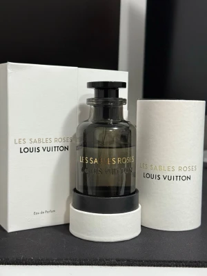 Louis Vuitton Les Sables Roses Eau de parfum 100ml - Exklusiv parfym från Louis Vuitton, Les Sables Roses. Flaskan är mörkgrå med svart lock och elegant rund form. Kommer i lyxig vit förpackning med guld- och svart text. Eau de Parfum, 100 ml.