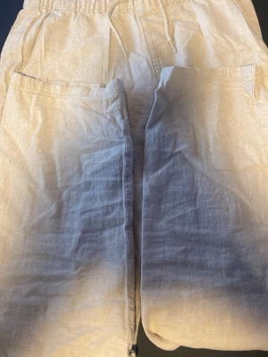 Beige mjukisbyxor med dragsko - Säljer ett par beige mjukisbyxor med resår i midjan och dragsko. Byxorna har två sidofickor och är tillverkade i ett mjukt, bomullsliknande material. Perfekta för chill dagar hemma eller när du vill ha det extra bekvämt. Köp innan sommarn börjar så att du hinner få ett par. Kan diskutera om pris