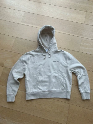 Beige hoodie från Axel Arigato - Säljer en stilren beige hoodie från Axel Arigato med tryck på bröstet och stor text på ryggen. Hoodien har huva med dragsko, magficka och ribbade muddar. Perfekt för dig som gillar minimalistisk streetwear och vill ha något bekvämt och snyggt. Tröjan har ett pytte litet hål på bröstet som knappt syns men annars är tröjan i topp skick. Tveka inte att höra av er vid frågor!! Ny pris 1800kr mitt pris 425kr. Tröjan är i Women S och liten i storleken.