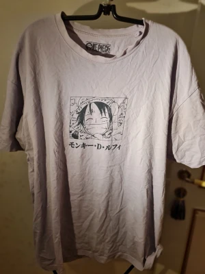 One Piece x Pull&Bear t-shirt XL - Ljuslila t-shirt från Pull&Bear med One Piece-tryck framtill som visar Luffy i manga-stil. Oversized passform och korta ärmar. Perfekt för animefans som vill ha en unik och bekväm tee med japansk text och cool design.