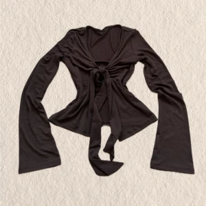 Brun omlottopp med knyt - Trendig brun omlottopp med långa ärmar och knyt framtill. Toppen har en djup v-ringning och vida ärmslut som ger en snygg retrovibe. Perfekt att styla över ett linne eller bh-top. Mjuk och stretchig känsla.