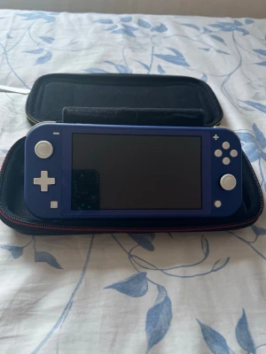 Blå Nintendo Switch Lite med Super Mario-väska - Säljer en blå Nintendo Switch Lite med vit-knappar och en Super Mario-väska med färgglatt motiv av klassiska karaktärer. Konsolen är kompakt och smidig, perfekt för gaming on-the-go. Väskan har handtag och dragkedja för enkel transport.