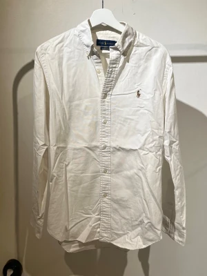 Vit skjorta från Ralph Lauren - Klassisk vit skjorta från Ralph Lauren i slim fit med stretch. Skjortan har button-down krage, broderad logga på bröstet och knappar framtill. Perfekt till både jeans och chinos för en clean och stilren look. (Behöver strykas en gång😅😅)