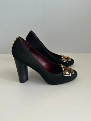 Marc by Marc Jacobs pumps i äkta läder, 40 - Helt otroliga, unika svarta pumps från Marc by Marc Jacobs i äkta läder. Storlek 40. Skorna har en elegant design med dekorativa utsmyckningar framtill och coola guldiga nitar baktill. Perfekt för både vardag och fest. Riktiga Power-shoes som får en att känna sig som den tuffa Boss Ladyn man är.   Mycket fint skick! Nypris 4000:-  Skickas mot porto eller hämtas i Stockholm. 