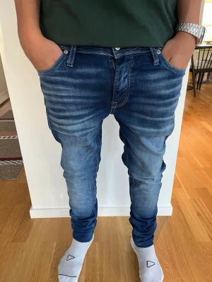 Blå slim fit jeans från Jack & Jones  - Säljer ett par blå slim fit jeans från Jack & Jones  med snygg tvätt och stretchigt material. Jeansen har klassiska fem fickor, låg midja och smala ben. Perfekta för dig som gillar en modern och tajt look.