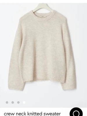 Beige stickad tröja med rund hals - Mysig beige stickad tröja med rund halsringning och ribbade muddar. Tröjan har en avslappnad passform och är perfekt för lager-på-lager. Materialet känns mjukt och fluffigt, vilket gör den extra skön att bära.