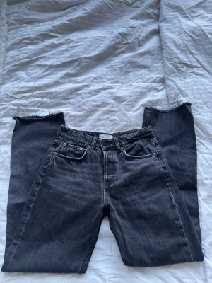 Svarta raka jeans från ZARA - Säljer ett par svarta/mörkgrå midwaist jeans från ZARA med råa, avklippta benslut. Klassisk femficksmodell och med en innerbenslängd på ca 76 cm. Jeansen är i denim och har en cool, avslappnad vibe som passar perfekt till sneakers eller boots✨