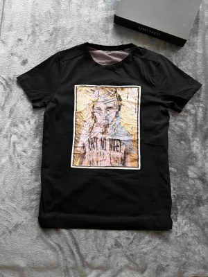 Svart t-shirt från limitato - Cool svart t-shirt från Limitato med ett stort grafiskt tryck på bröstet i lila, beige och svart. Klassisk passform och rund halsringning. Perfekt för dig som vill sticka ut med din stil.