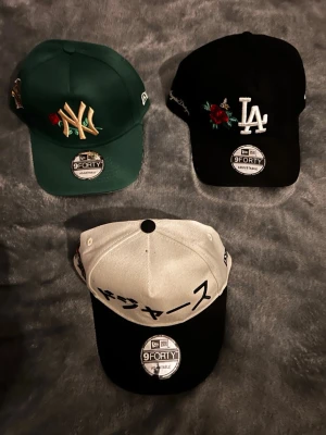 New Era kepsar  - 200kr per keps !    Tre snygga New Era 9FORTY kepsar: en grön med NY-brodyr och ros, en svart med LA-brodyr och rosdetalj samt en vit/svart med japansk text. Alla har böjd skärm och justerbar passform. Perfekt accessoar för att lyfta din streetwear-stil.
