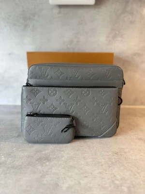 Grå Louis Vuitton handväska i läder - Grå handväska från Louis Vuitton i präglat läder med ikoniskt monogrammönster. Väskan har en rektangulär form och en matchande liten pouch som kan fästas på väskan. Perfekt för dig som gillar exklusiva och stilrena accessoarer.